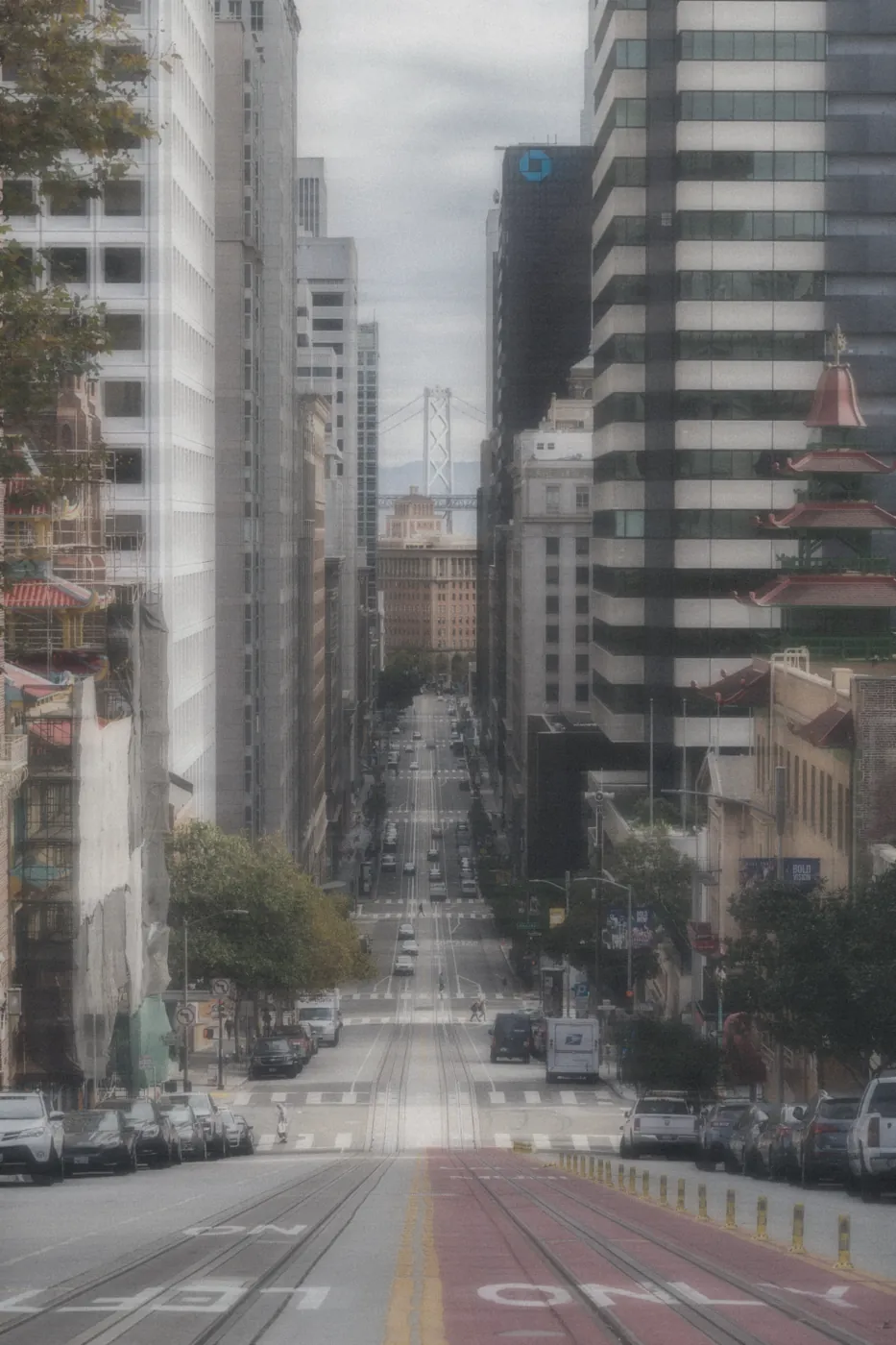 A steep San Francisco street framed by downtown towers, the Bay Bridge in the distance