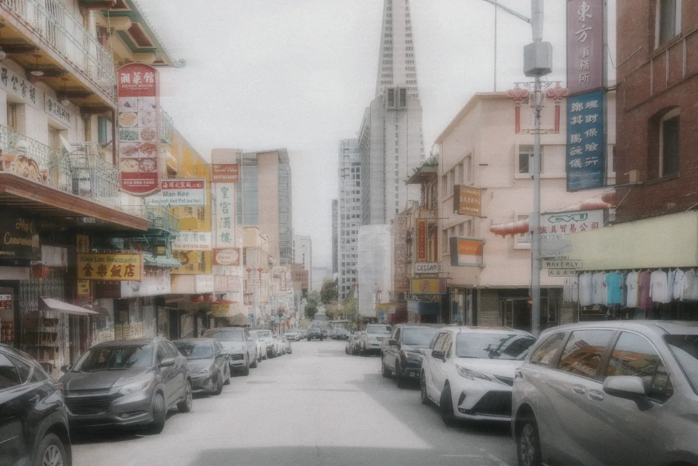 A Chinatown street lined with signs and parked cars under a soft overcast sky