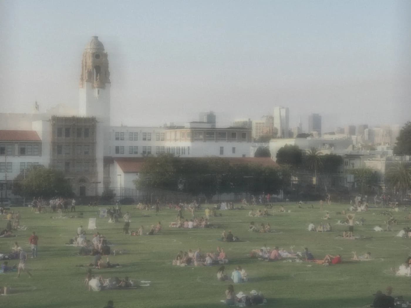 Crowds relaxing on the grass at Dolores Park with the city skyline behind